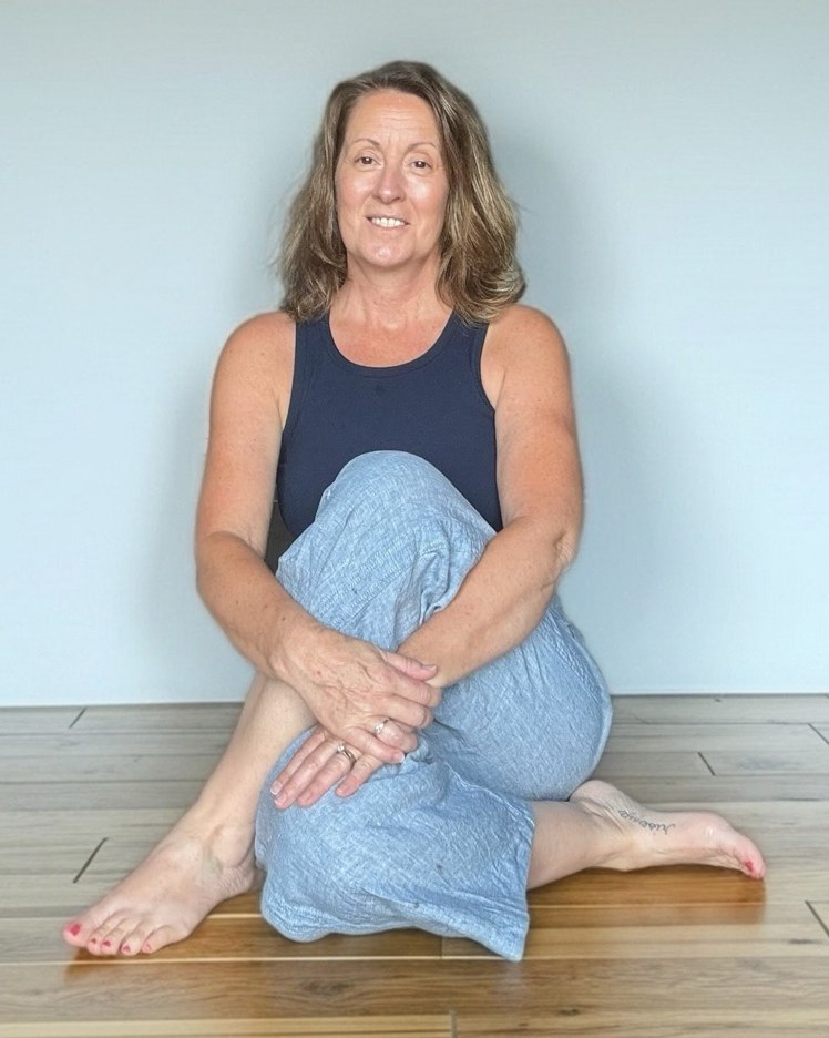 Lisa Segar seated on a wood floor in front of a soft white wall, smiling warmly.